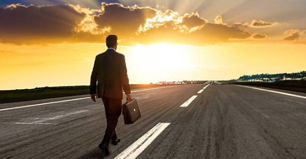 Man in business attire with a briefcase walking on a road into a sunrise