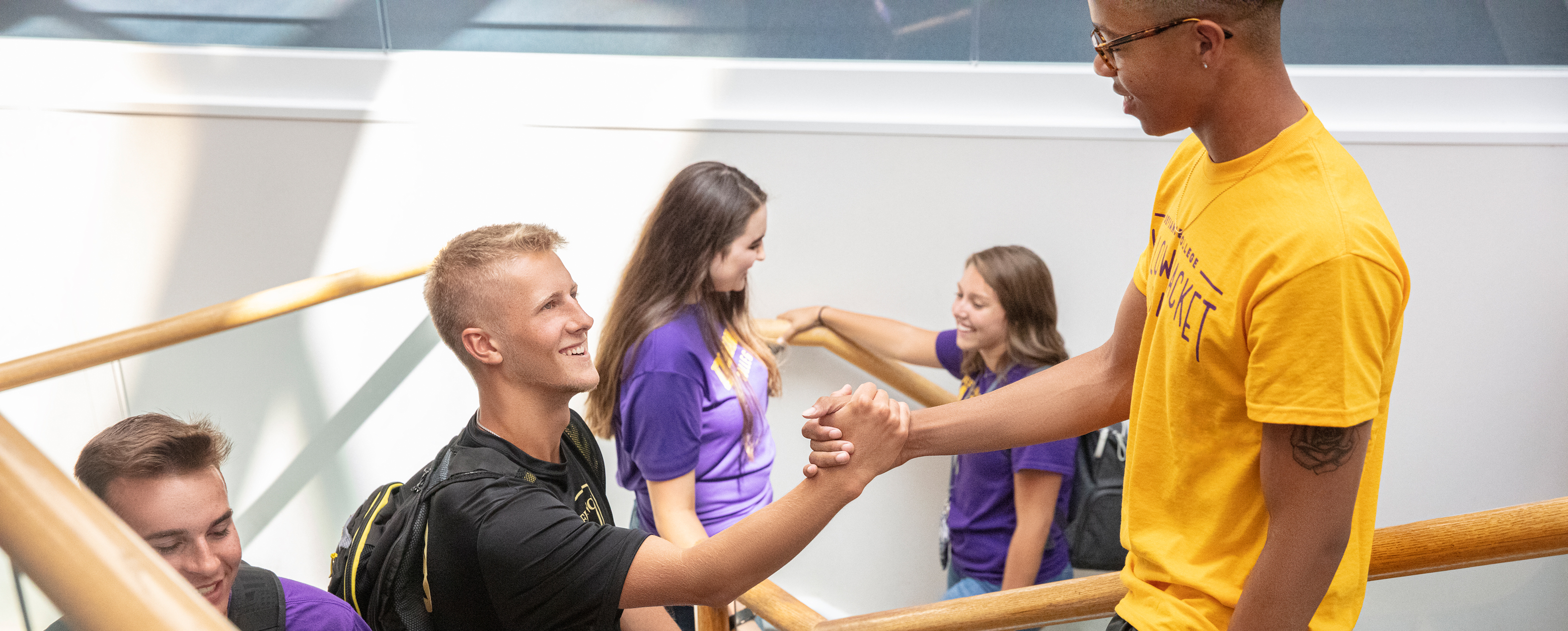 Five students passing by one another and talking on a stairwell - three male and two female students.