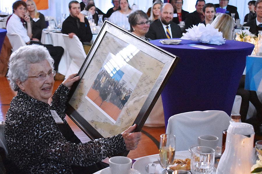 Woman holding framed photo of people with multiple seated guests in background