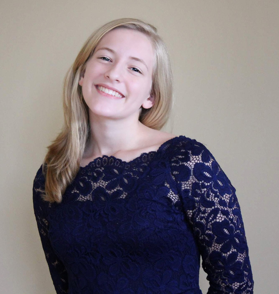 Young blonde girl in a dark navy lace shirt smiling at the camera