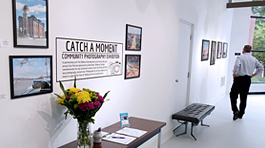Large photos of scenes in the city of Defiance are hanging on the gallery wall. A table with flowers and a guestbook are sitting against the wall.