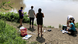 Five women standing near the Maumee river bank with equipment to test the water.