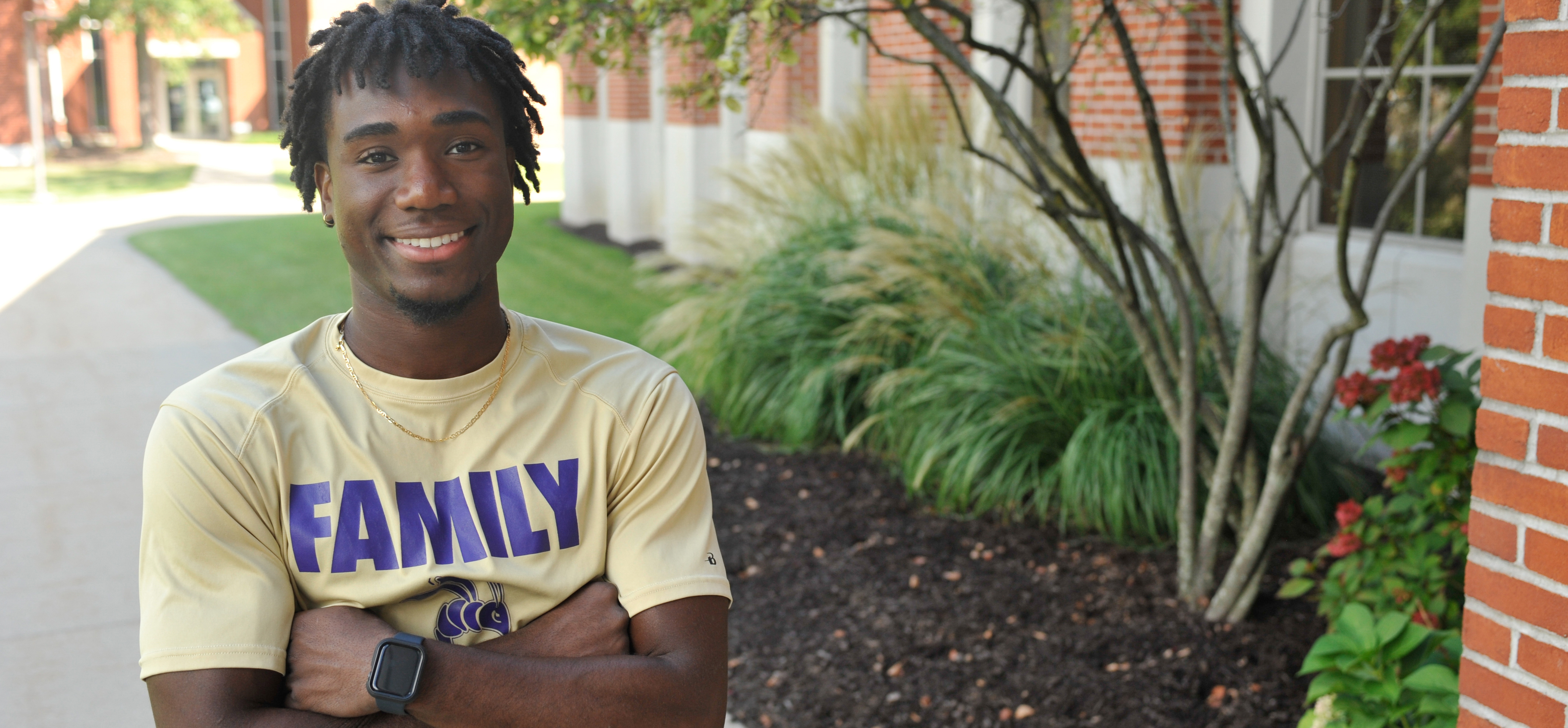 male student smiling at the camera with arms crossed