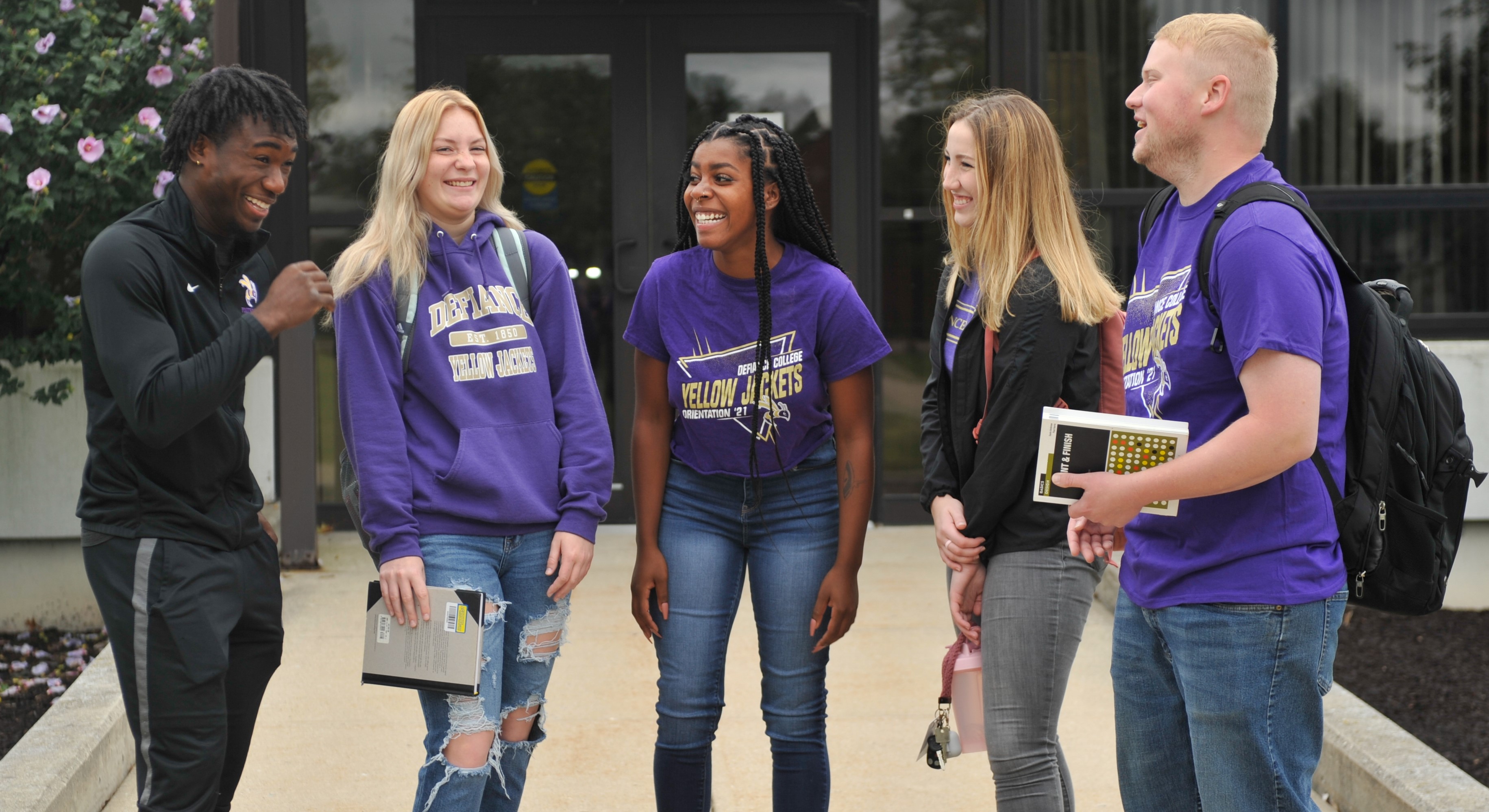 group of 5 students talking to each other laughing