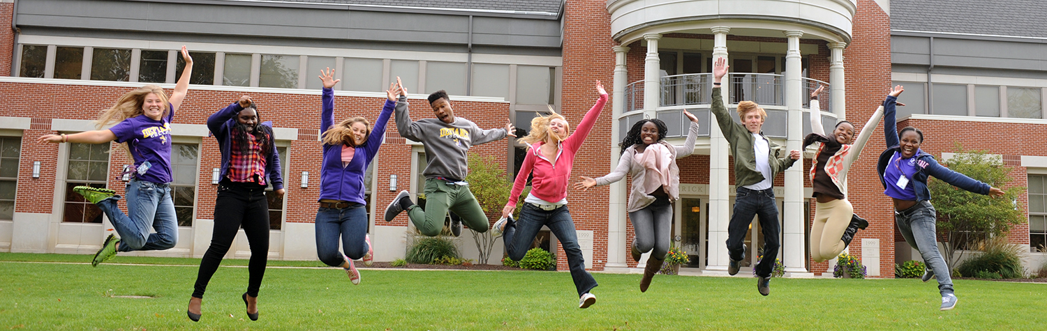Nine students jumping for joy in front of Serrick Campus Center building