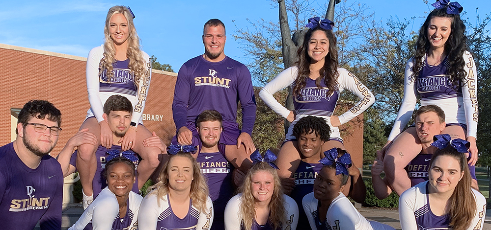 14 students in Defiance College cheer shirts and outfits gathered together and smiling at the camera