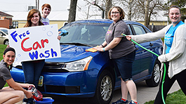 Five band members washing a blue car and holding a sign that says Free Car Wash