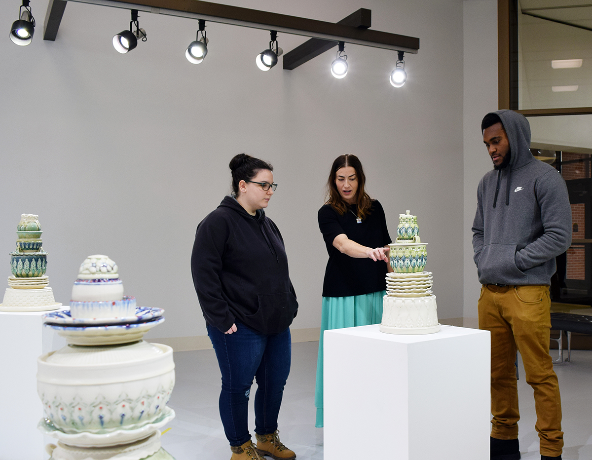 Professor Beverly Fanning looking at ceramic sculptures in the art gallery with two students