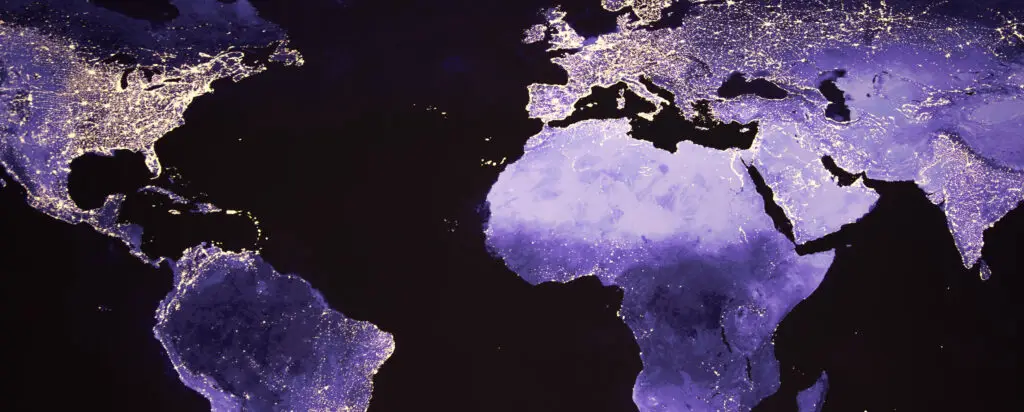 Satellite view of Europe, Africa, and the Americas at night, showing city lights highlighting population centers across the continents against a dark background.